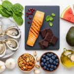 Twelve superfoods arranged on marble surface including oysters, salmon, nuts, and dark chocolate that boost testosterone and sexual health in men over 30